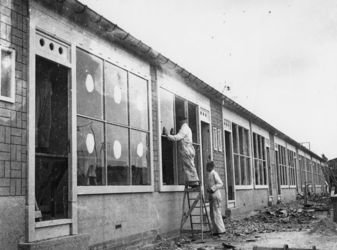 1977-3214 Glazenzetters aan het werk bij noodwoningen van het Brabants Dorp. De nieuwe ruiten worden gemarkeerd met ...